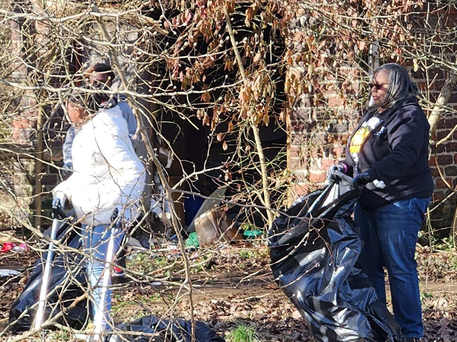 Two volunteers in gloves bagging litter from a brushy Dayton lot
